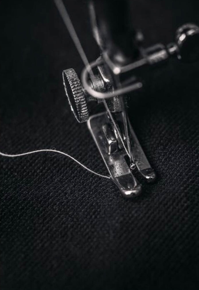 Close-up of a sewing machine needle and thread on a dark fabric background